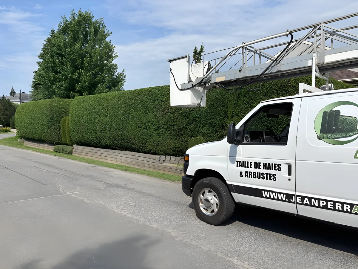 Le camion lettré et la nacelle de Jean Perrault devant une longue haie de cèdres fraîchement taillée